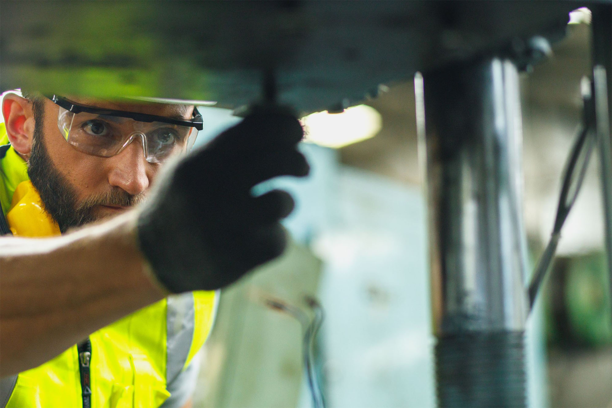 Industrimontör i skyddsglasögon och reflexväst justerar en maskindel
